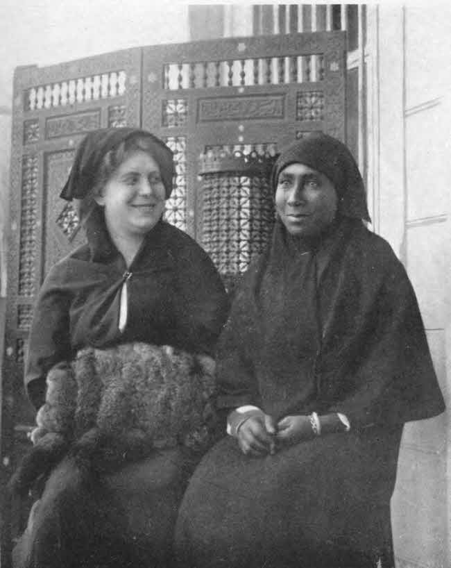  The author is shown seated with
Miss Chocolate, both in long covering attire with their hair covered.